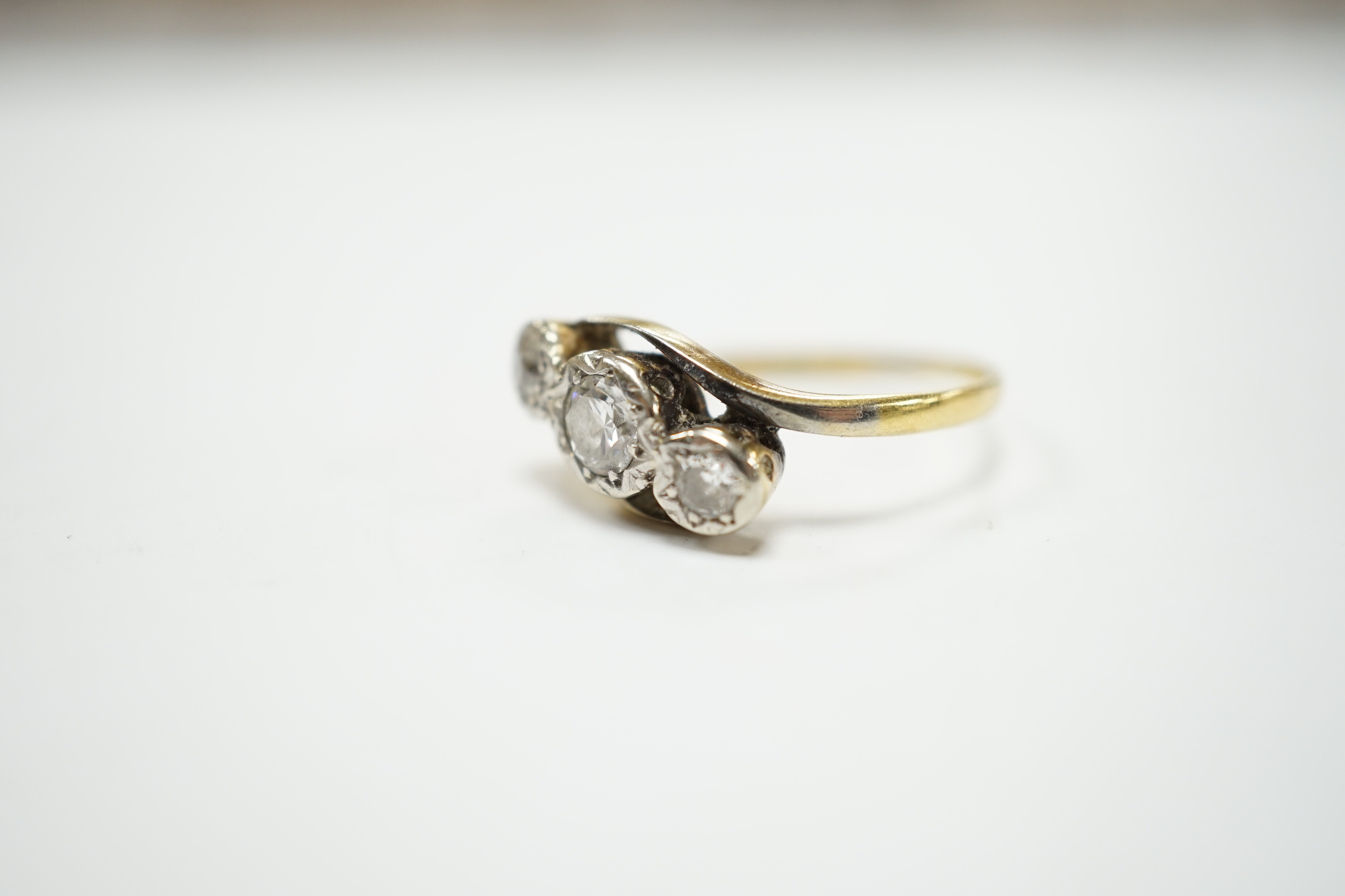 A yellow metal and illusion set three stone diamond set crossover ring, size O/P, gross weight 3.2 grams.